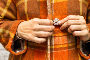  A woman buttoning her coat, close-up. A woman unbuttons her coat. women's fingers fastening a button. woman putting on coat. woman trying on coat. autumn coat. checked coat. 