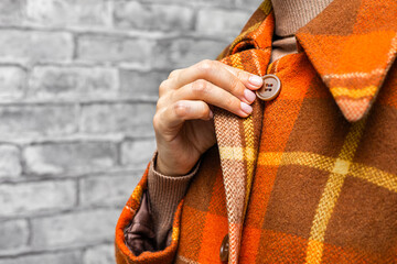  A woman buttoning her coat, close-up. A woman unbuttons her coat. women's fingers fastening a button. woman putting on coat. woman trying on coat. autumn coat. top button. checked coat