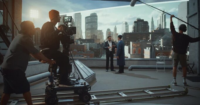 Male Camera Operator Rides a Dolly on Rooftop Film Set, Actors Play in Dramatic Dialogue Scene. Using Virtual Production and to Achieve Smooth Cinematic Movement and Visual Storytelling Aesthetics