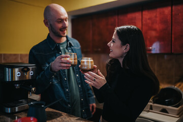 A man and a woman toast with coffee drinks in a home kitchen. They share a warm moment near a sleek espresso machine.
