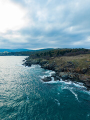 Obraz premium Waves crashing against rocky shoreline under a cloudy sky at dusk by the coast