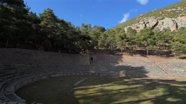 Delphi temple 4k video. Panoramic view of the ancient Greek theater of Delphi built into the rocky mountainside, overlooking a deep green valley under a clear blue sky.