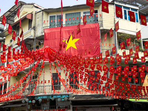 View of vibrant red Vietnamese flags flutter amidst the weathered facades of buildings, creating a striking scene of cultural pride, Hanoi, Hanoi, Vietnam.