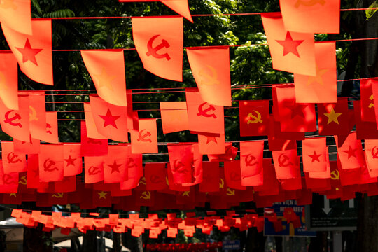 View of vibrant red flags bearing communist symbols flutter overhead, creating a striking display against the lush green canopy, Hanoi, Hanoi, Vietnam.