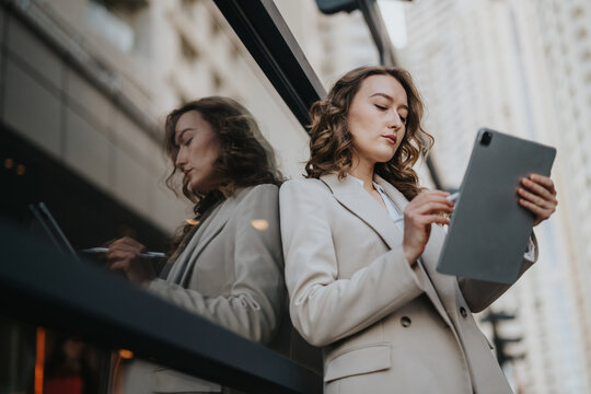 A businesswoman in a light blazer stands outside a modern building, focused on a tablet. Colleagues are implied in the urban setting, though not shown.