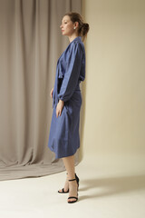 Female model wearing monochrome denim blue outfit. Midi skirt and bow-tie neck blouse. Fashion studio shot.