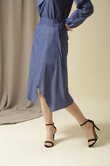 Female model wearing monochrome denim blue outfit. Midi skirt and bow-tie neck blouse. Fashion studio shot.