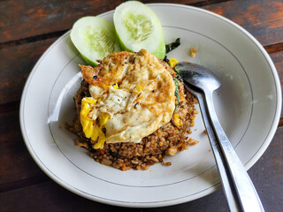 Fried rice with egg and vegetables in a white plate, at an outdoor stall during the day.