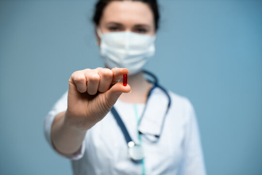 Female medical doctor in mask holding red pill with stethoscope visible on blue background