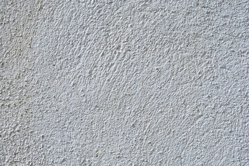 A close-up shot captures the rough, uniformly coarse texture of a white or light gray stucco wall surface under natural light