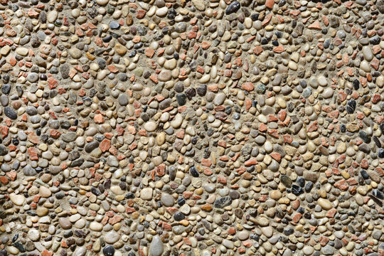 A close-up shot captures the rough, exposed aggregate texture of a wall or concrete surface composed of small, multicolored pebbles and stones
