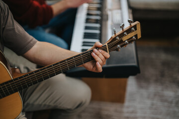 Fototapeta premium A guitarist plays a warm acoustic guitar while a keyboard and amp sit nearby in a casual practice scene.
