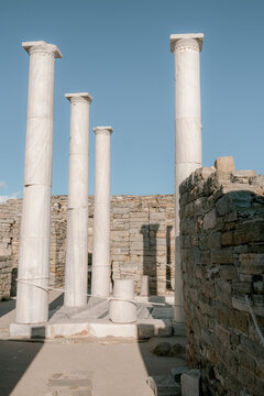 Scenic view of Delos island featuring ancient Greek ruins, standing columns, scattered marble blocks illuminated by warm summer light.