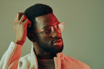 Thoughtful young African man in glasses with a pensive expression, wearing a cozy sweater against a muted gradient background reflecting introspection and style