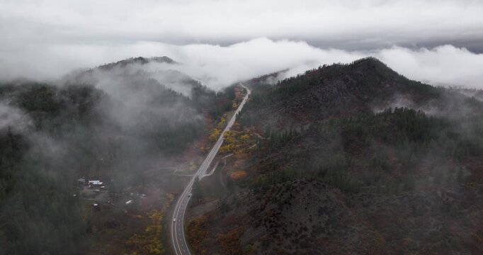 Aerial drone shot tracking forward along the scenic Route 160 in Colorado, with low-lying clouds and fog sporadically covering the vibrant autumn foliage showcasing the beauty of fall in the Rockies.