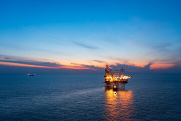 Fototapeta premium Aerial view from a drone of big jack up offshore drilling oil rig, production platform and supply vessel In the ocean during sunset - Oil and Gas Industry