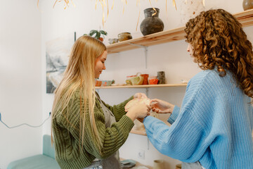 Two friends gather in a cozy pottery studio, crafting unique pieces during a creative workshop. Natural light floods the room, enhancing their artistic experience with clay and laughter.