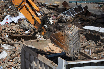 Excavator bucket loading debris into a dump truck, illustrating demolition, construction, and waste management process on a building site.