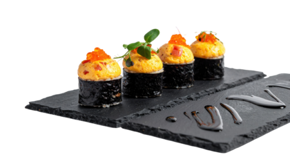 Four pieces of savory sushi on a dark slate board, with a black background. Each roll is topped with orange and green garnish