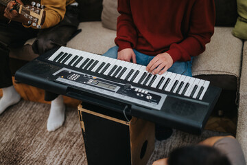 A person plays a keyboard while another strums a guitar in a cozy living room. Friends or family...