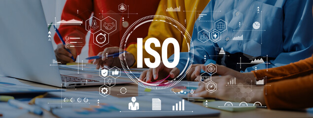 Team members engage in a collaborative discussion on ISO standards while analyzing data, charts, and documents in a modern office setting. Trope