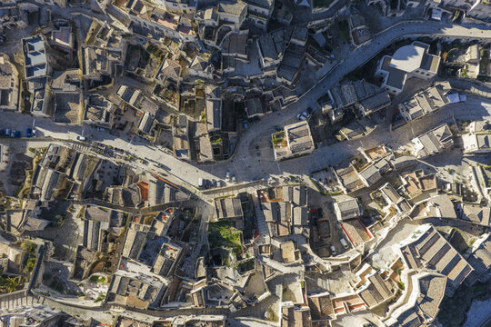 Aerial view of ancient dwellings cascade down sun-drenched slopes, casting long shadows over winding stone streets, a timeless tableau of history and architecture, Matera, Basilicata, Italy.