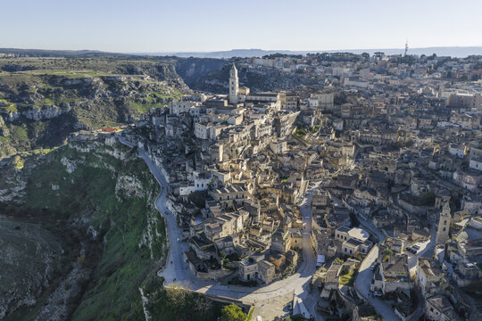 Aerial view of ancient stone dwellings cascading down the ravine, the Duomo's spire piercing the skyline in the Sassi di Matera, Matera, Basilicata, Italy.