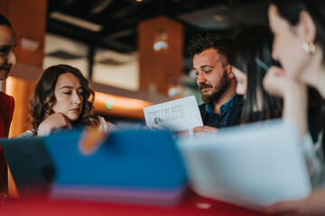 A team of colleagues gathers around a table, reviewing a chart and papers as they brainstorm ideas. Warm lighting and focused expressions create a collaborative, productive office atmosphere.