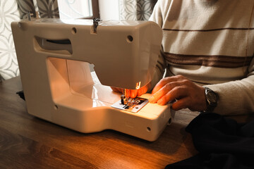 Senior person threading a needle on a modern white sewing machine.