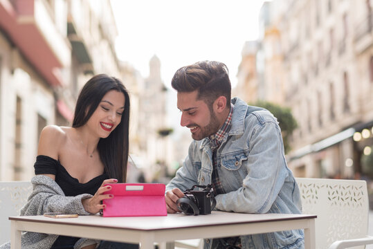Young couple reviews photography in digital tablet  while waiting drinks in bar terrace in city outdoors image