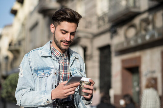 Young man drinking coffee to go and looking smartphone in the city