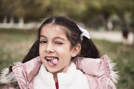 Little pretty girl looking at camera in park winter scene, tongue out
