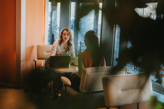 Two colleagues exchange ideas in a cafe setting, with a laptop on the table and warm natural light. A coworker listens and contributes, conveying collaboration, focus, and creative conversation.