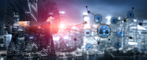 A business executive stands confidently against a vibrant cityscape, showcasing digital technology integration with graphical network connections and business icons. Tessel