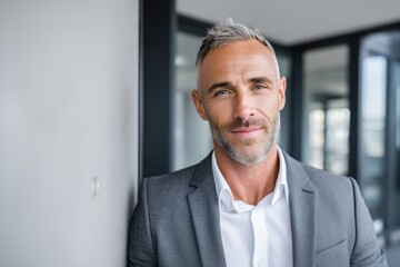 Fototapeta premium Professional male consultant in charcoal gray suit, leaning near wall in bright office, confident expression, consulting and finance services marketing