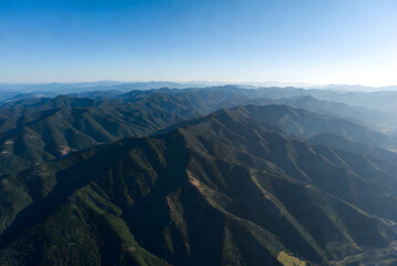 Aerial view of layered mountain ranges under a clear blue sky during daylight.