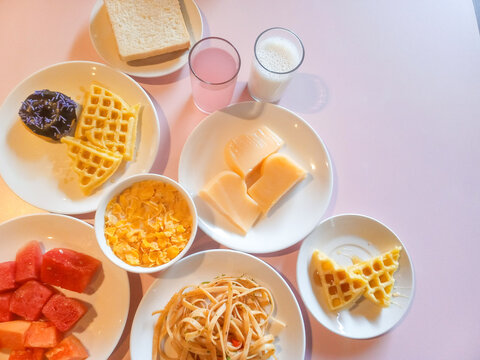 Food combination consist of waffle,noodle,bread,milk,cereal,papay fruit and puding. In pink background. Food photography.

