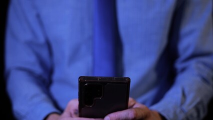 Businessman working late at night on mobile phone, typing email to colleagues