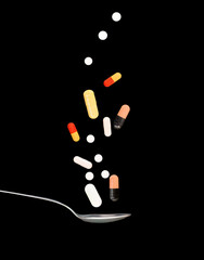 Selection of pills and capsules falling on to a spoon