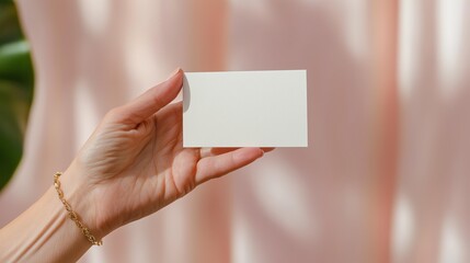 Minimalist mockup of female hand holding blank business card against soft pink background
