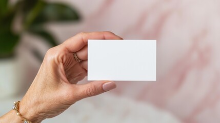 Hand holding blank business card against soft pink background for mockup design