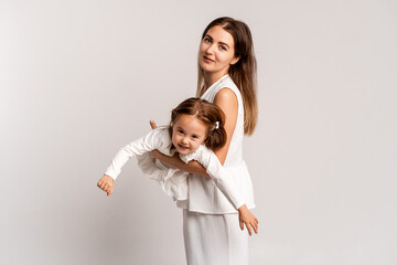 mother and child girl on a white cyclorama background, mother and daughter in a white suit hugging and kissing while playing, portrait, place and space for text