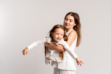 mother and child girl on a white cyclorama background, mother and daughter in a white suit hugging and kissing while playing, portrait, place and space for text