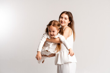 mother and child girl on a white cyclorama background, mother and daughter in a white suit hugging and kissing while playing, portrait, place and space for text