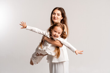 mother and child girl on a white cyclorama background, mother and daughter in a white suit hugging and kissing while playing, portrait, place and space for text