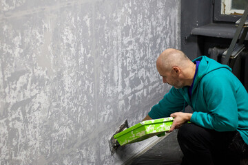 A skilled plasterer masterfully applies decorative plaster to a wall with a trowel and green container, demonstrating craftsmanship in interior design for artistic wall finishing, bringing unique