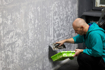 Man skillfully applies decorative plaster to a wall using a trowel, crafting a textured surface ideal for highlighting renovation, construction, or interior design projects, with a distinct artistic