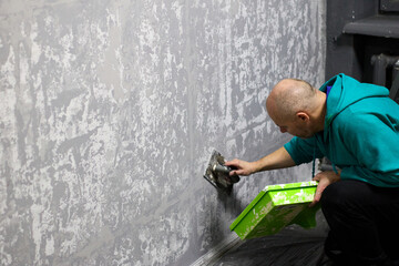 An experienced craftsman demonstrates expertise by skillfully applying decorative plaster to a wall with a trowel, construction and interior design, focused on the work site.