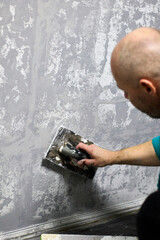 A bald man applies decorative plaster to a wall with a trowel, creating a unique, textured finish for a home improvement project, skill and artistry.