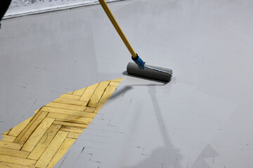 Renovating a parquet floor with gray paint using a paint roller: Highlighting worker's attention to detail in restoration, bringing new life to home, interior design.